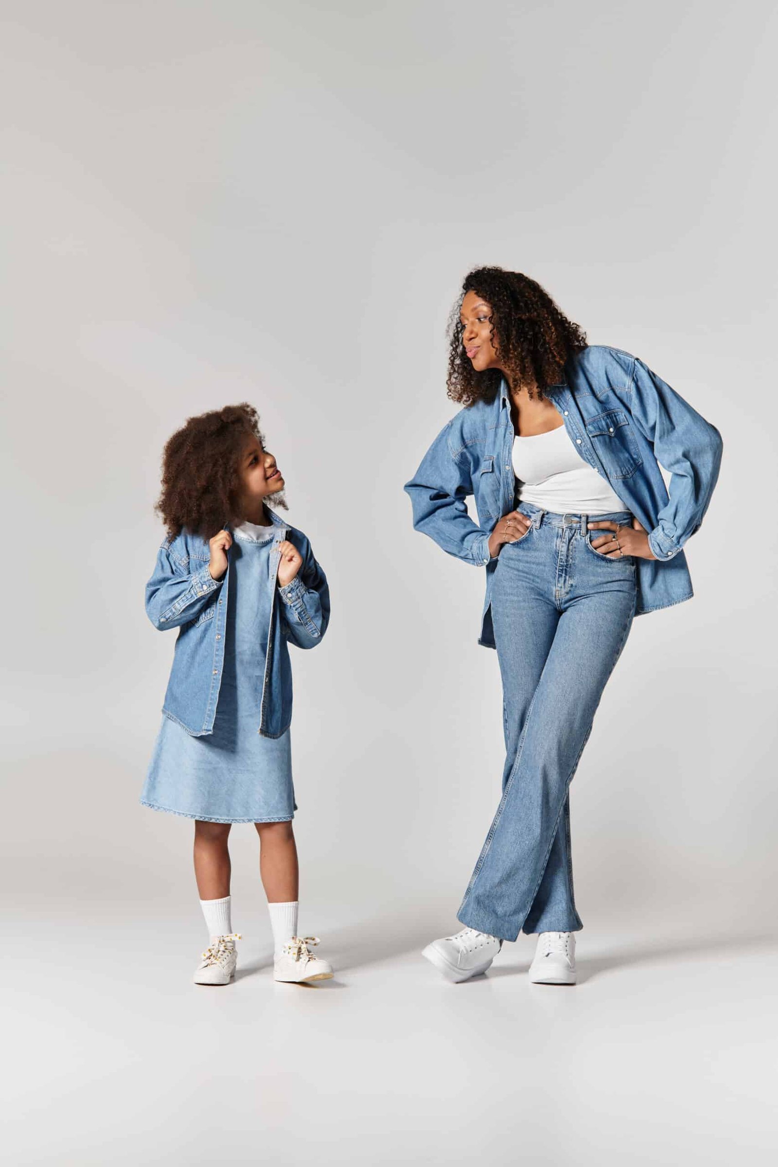 African American Mother and Daughter, both in denim, posing on grey background.